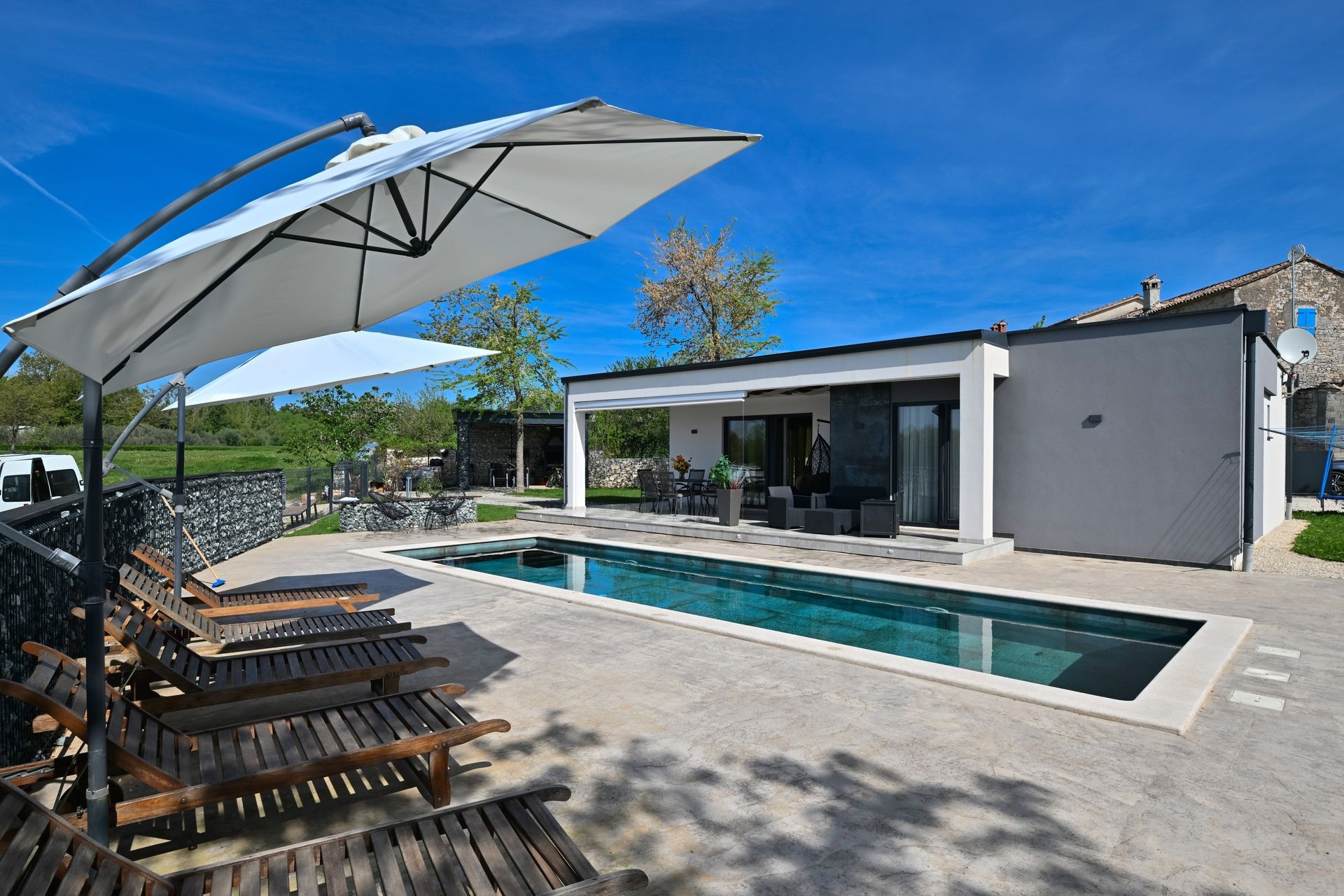 Moderner Bungalow mit rechteckigem Pool und mehreren Liegestühlen unter großen Sonnenschirmen auf gepflasterter Terrasse